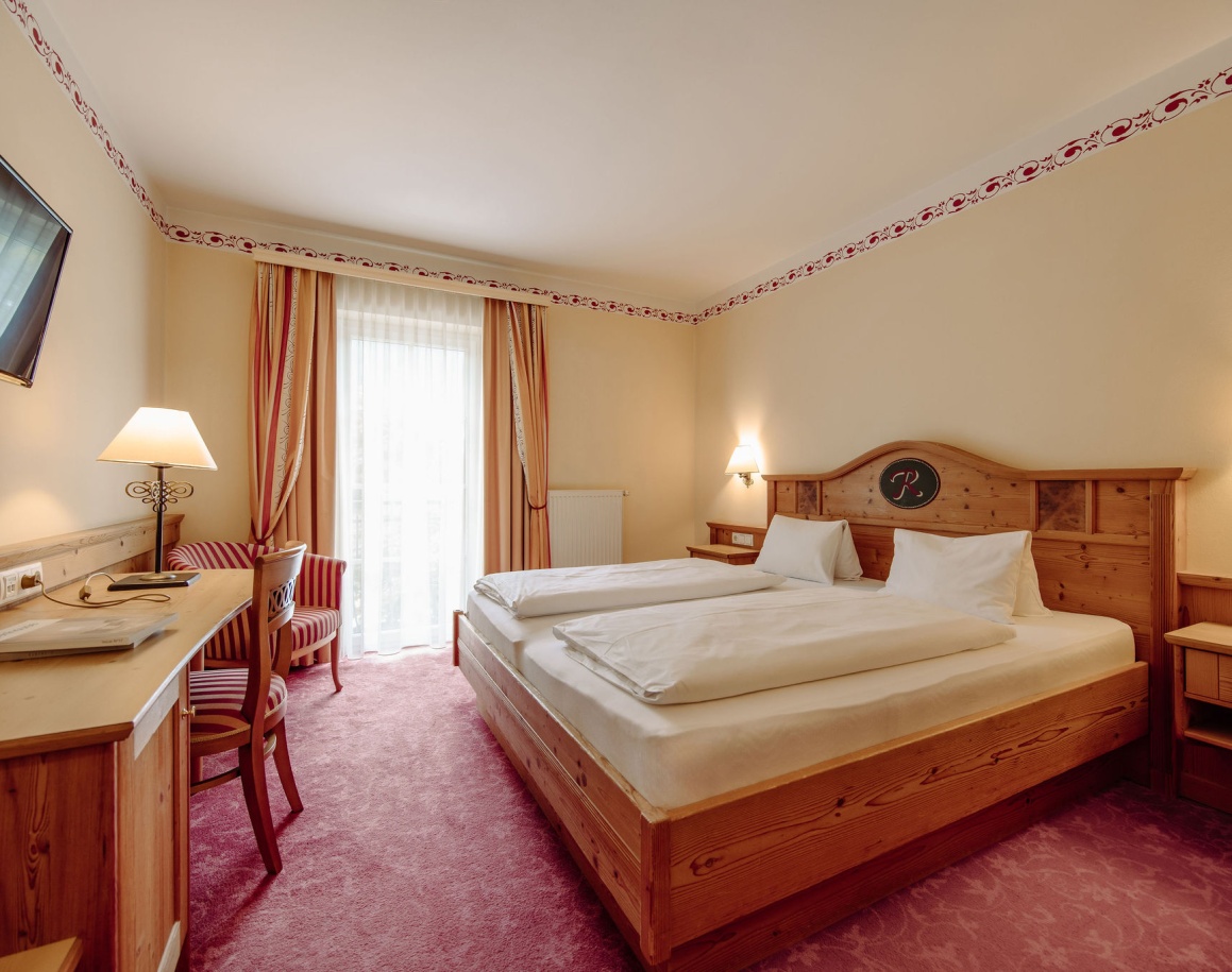 Helles Hotelzimmer mit Doppelbett, Schreibtisch, Stühlen und zwei Lampen