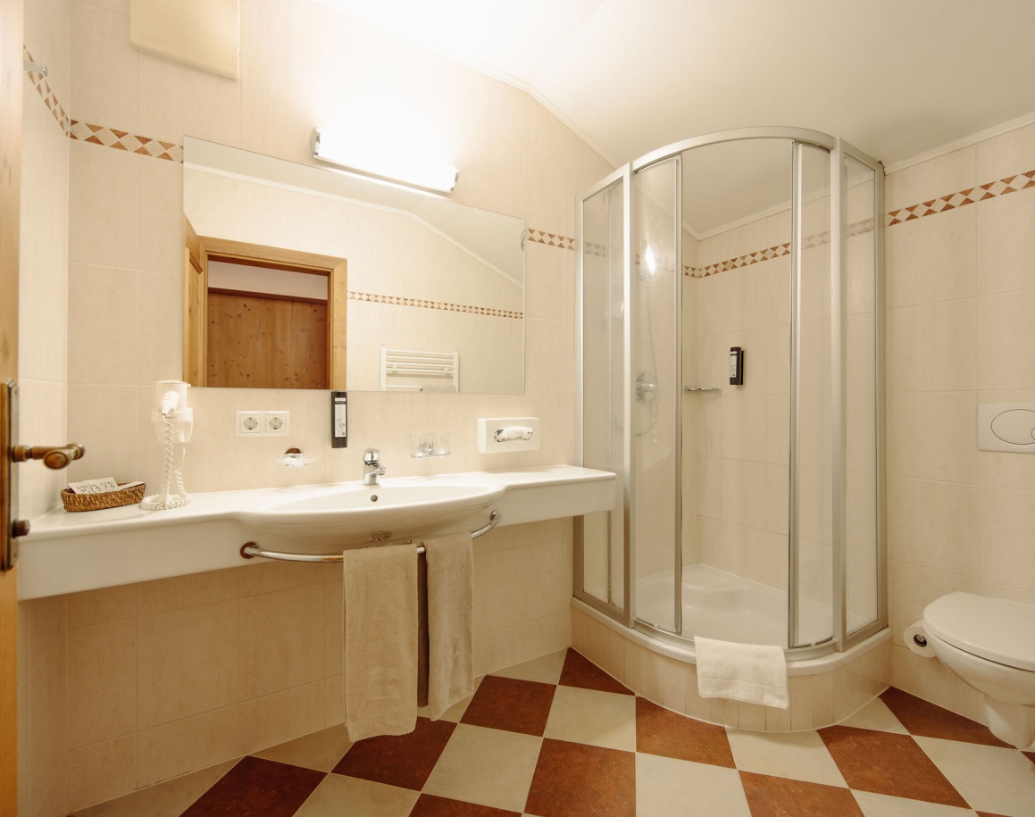 Helles Badezimmer mit großer Spiegelwand, Eckdusche und gemustertem Boden