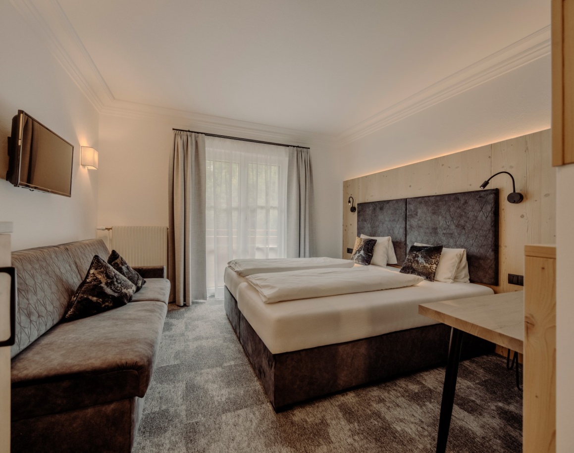 Gemütliches Hotelzimmer im Resl mit Doppelbett, modernem Dekor, Sofa und Fernseher in Flachau
