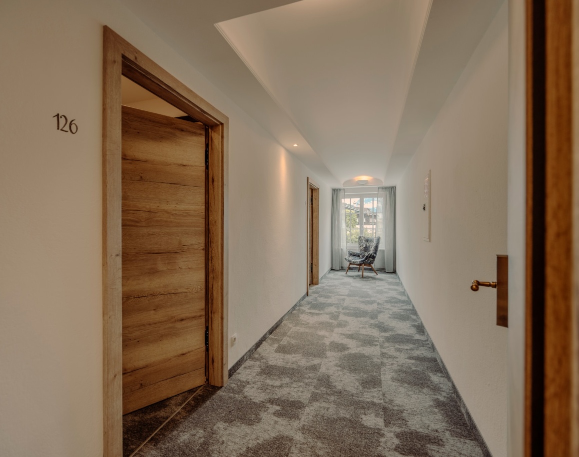 Ein langer, schmaler Flur mit Türen und einem Fenster am Ende, durch das Licht scheint