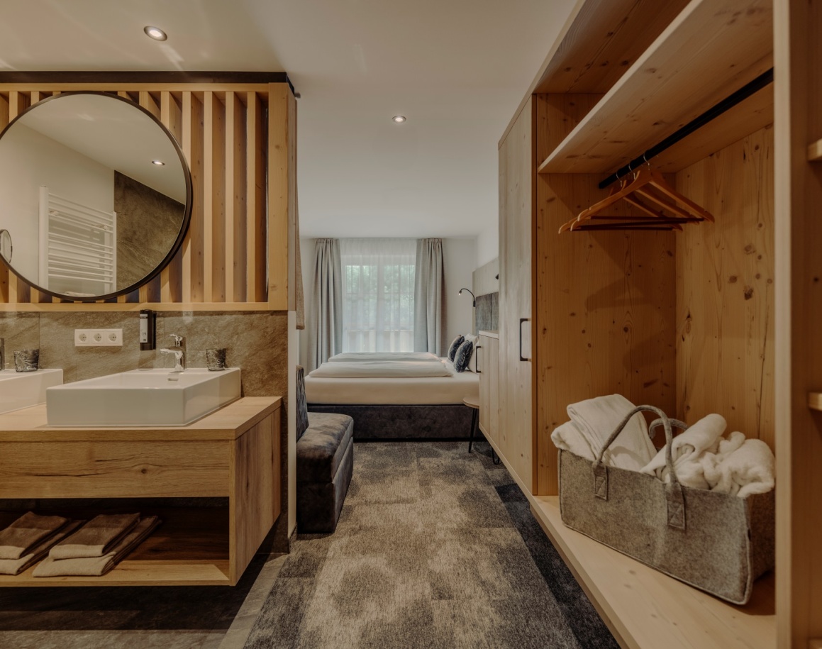 Ein modernes Hotelzimmer mit Doppelbett, offenem Schrank und Badezimmerbereich