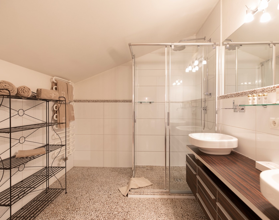 Modernes Badezimmer mit Dusche, Waschtisch, beleuchtetem Spiegel und Regal mit Handtüchern