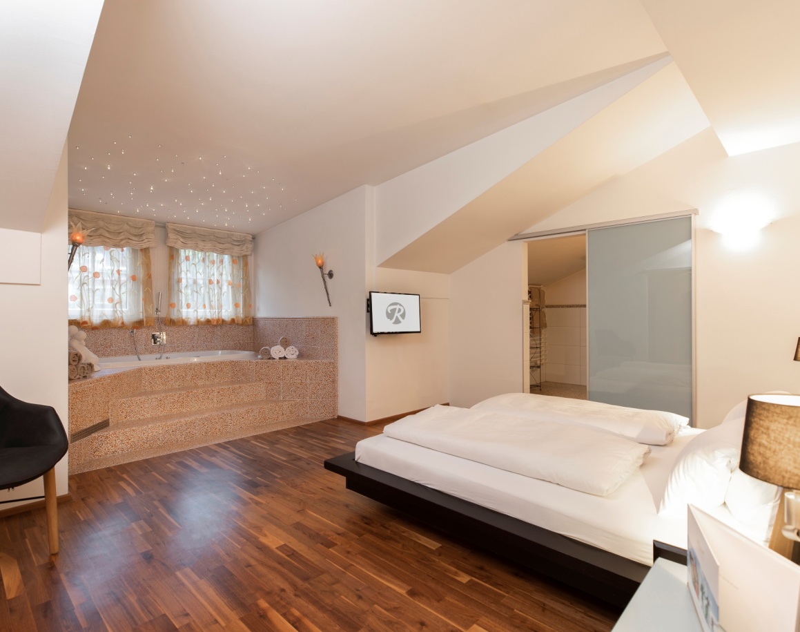 Gemütliches Schlafzimmer mit Holzfußboden, großem Bett und Badewanne im Hotel Resl