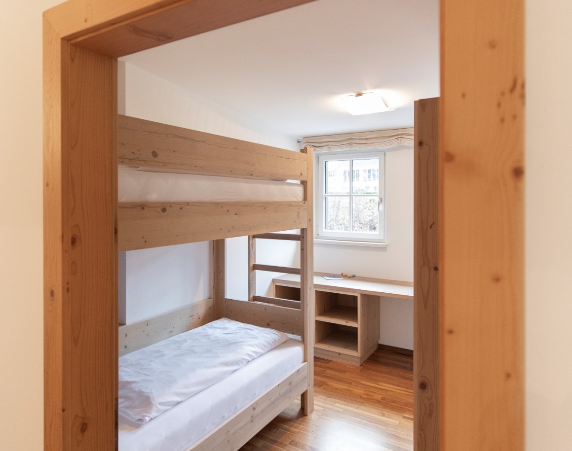 Holz-Etagenbett und Schreibtisch in einem hellen Zimmer mit Fenster